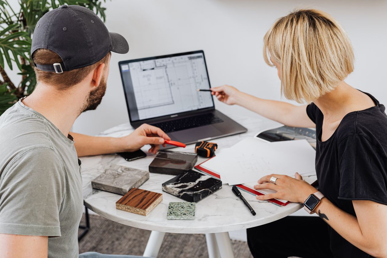 Two designers reviewing building plans and design samples in a modern office setting