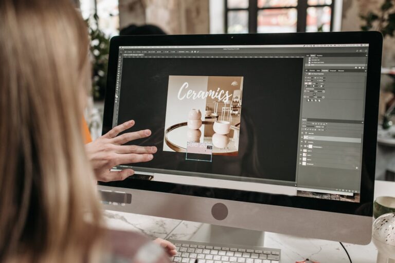 Graphic designer working at a computer with Adobe Photoshop design software on screen