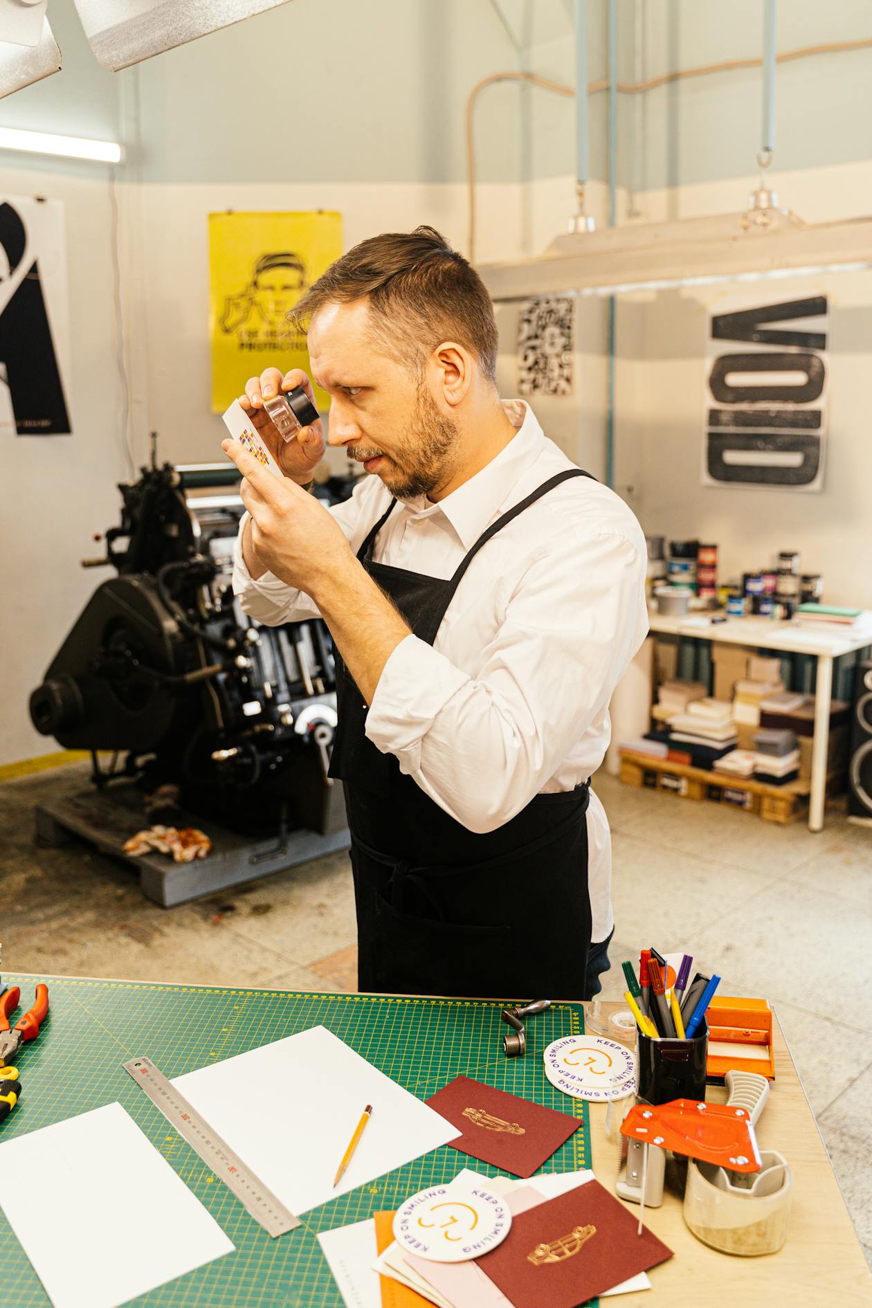 Graphic designer examining printed materials with a magnifying glass for quality inspection in a studio