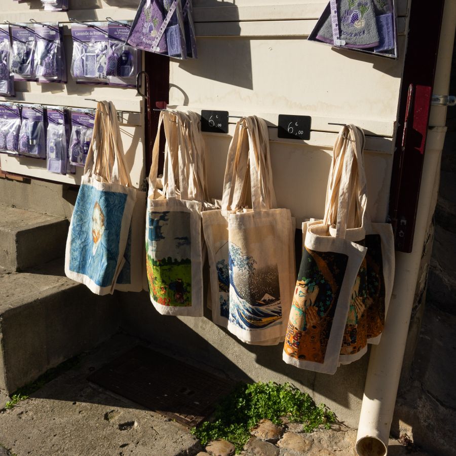 Printed canvas tote bags with artwork designs on display outside a shop