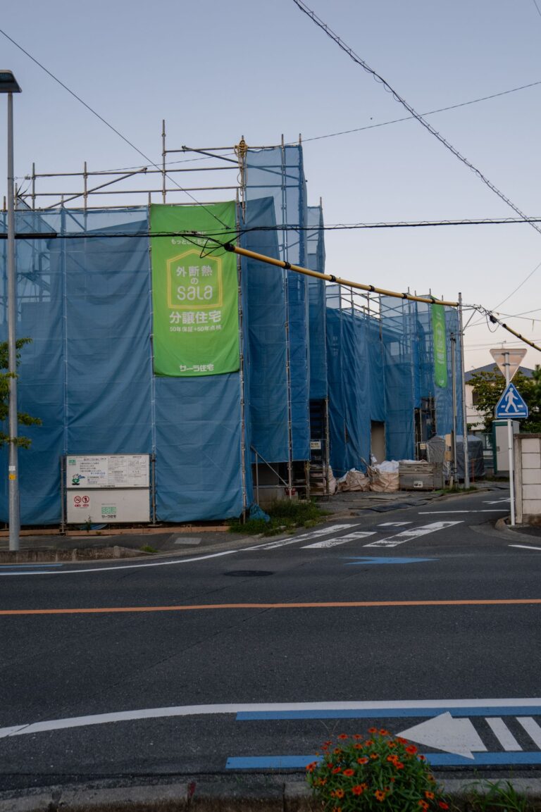 Street view of a construction site enclosed in blue mesh safety netting