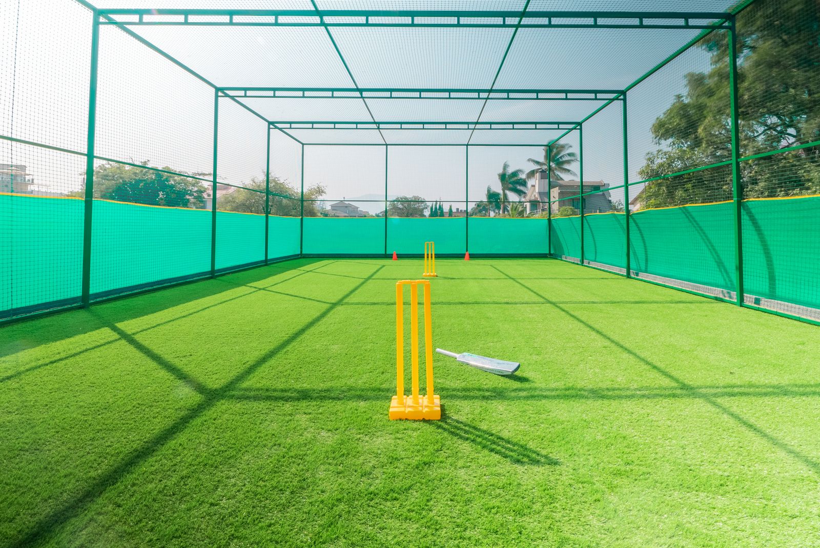 Cricket practice net with bright yellow stumps on a sunny day