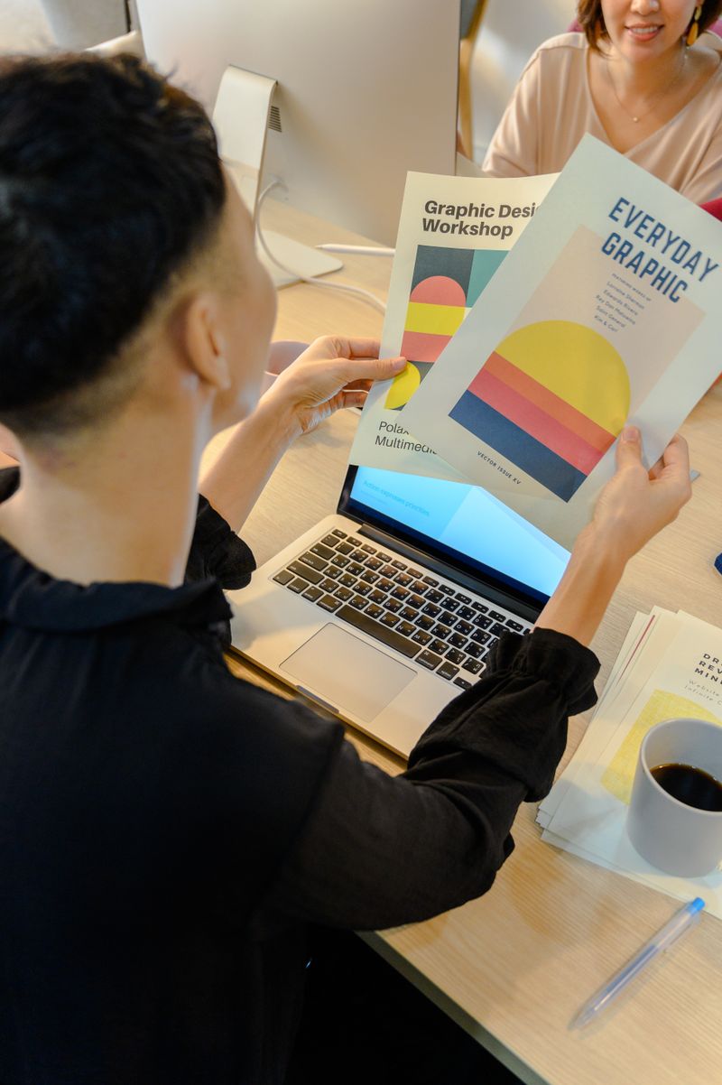 Designer reviewing printed design proofs beside a laptop