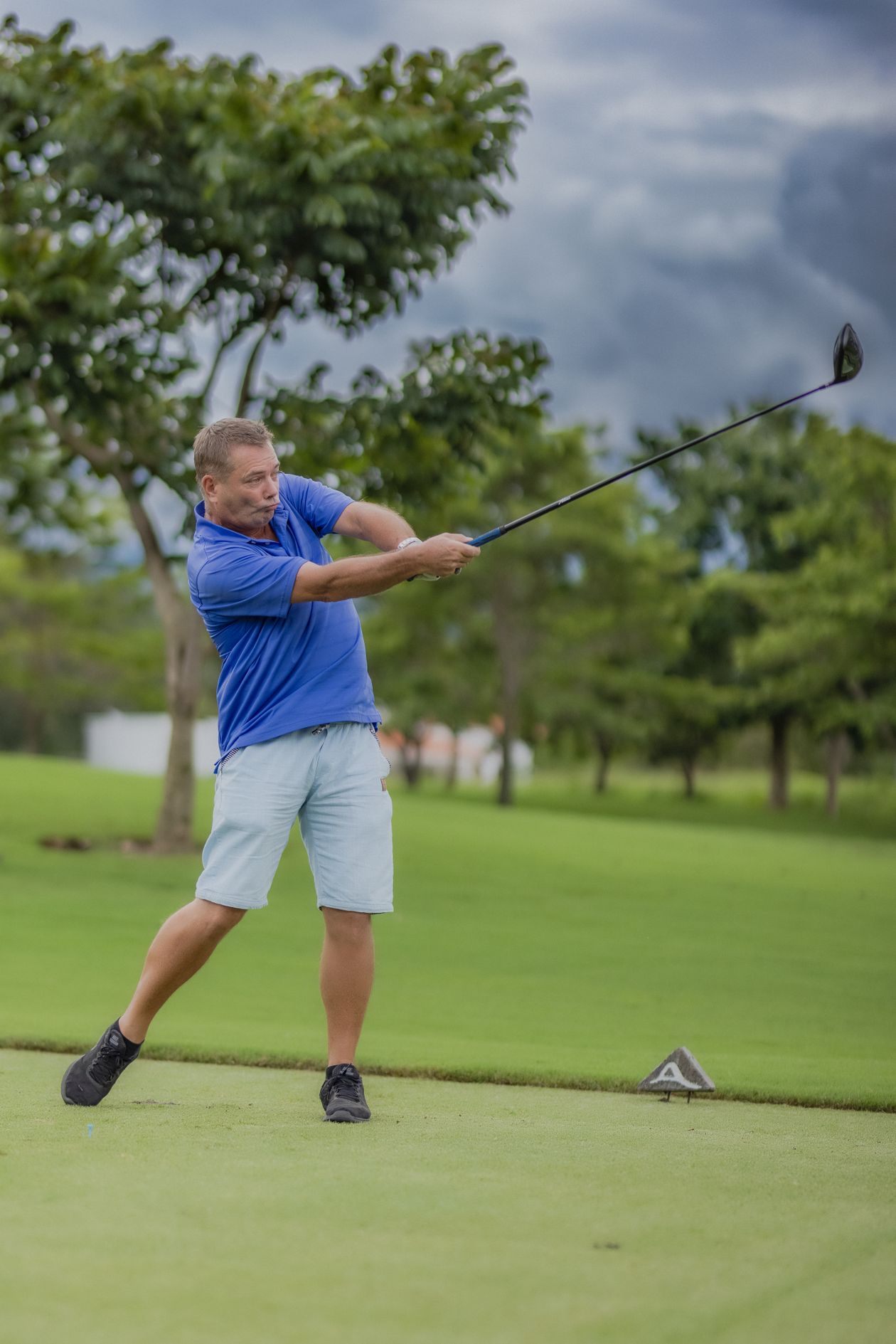 Golfer in a blue polo shirt mid-swing on the course