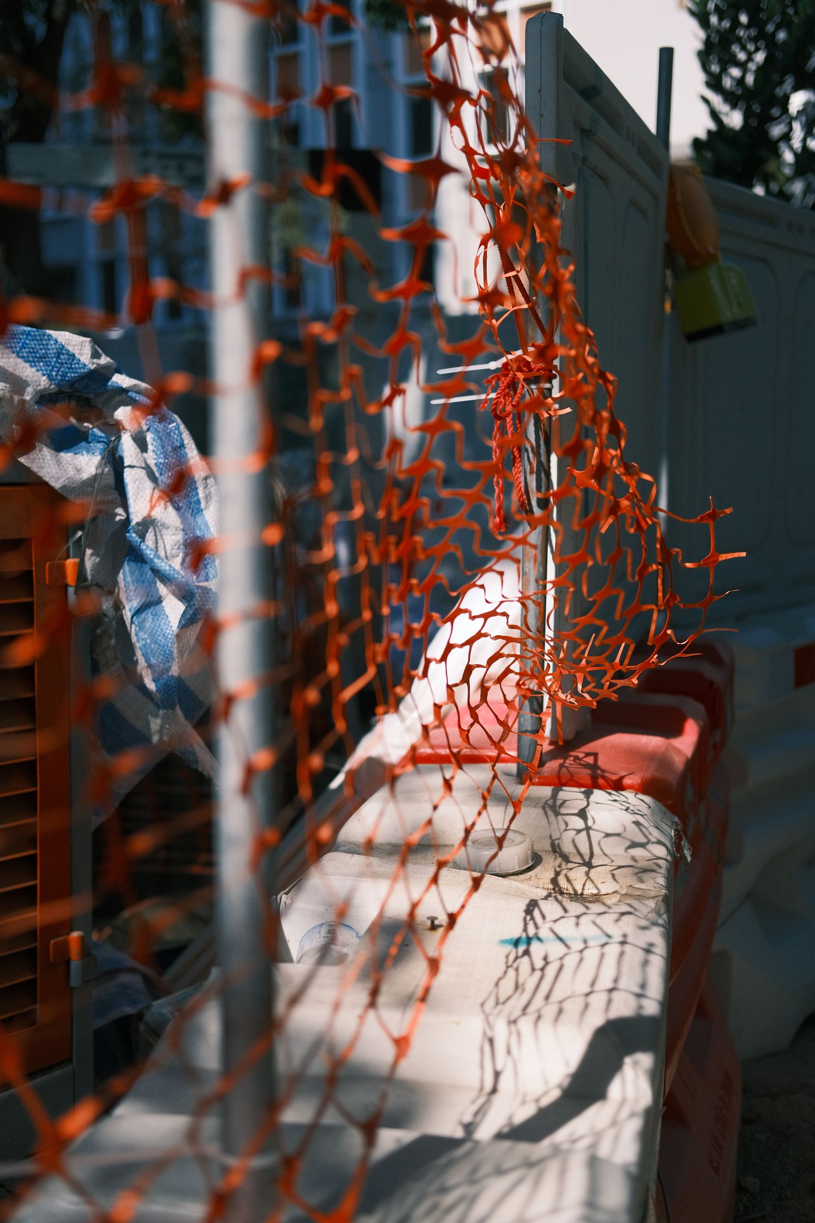 Orange safety netting fencing at a construction site with geometric shadow patterns