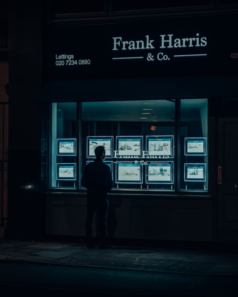 Silhouette of a man viewing illuminated property listings in a window at night