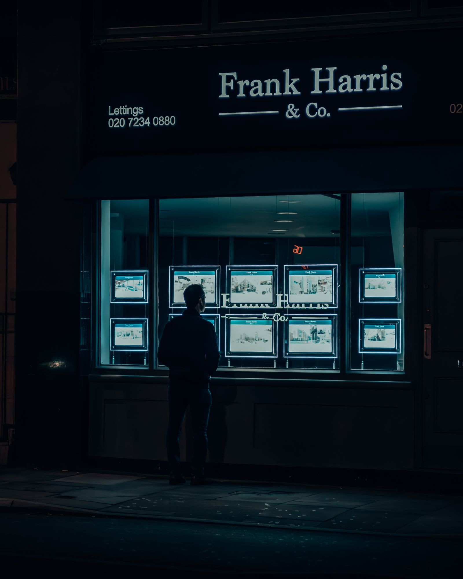 Silhouette of a man viewing illuminated property listings in a window at night