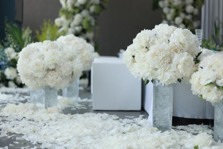 White floral arrangements and scattered petals at a wedding aisle