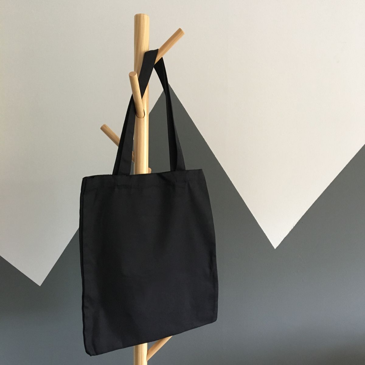 Plain black canvas tote bag hanging on a wooden coat rack