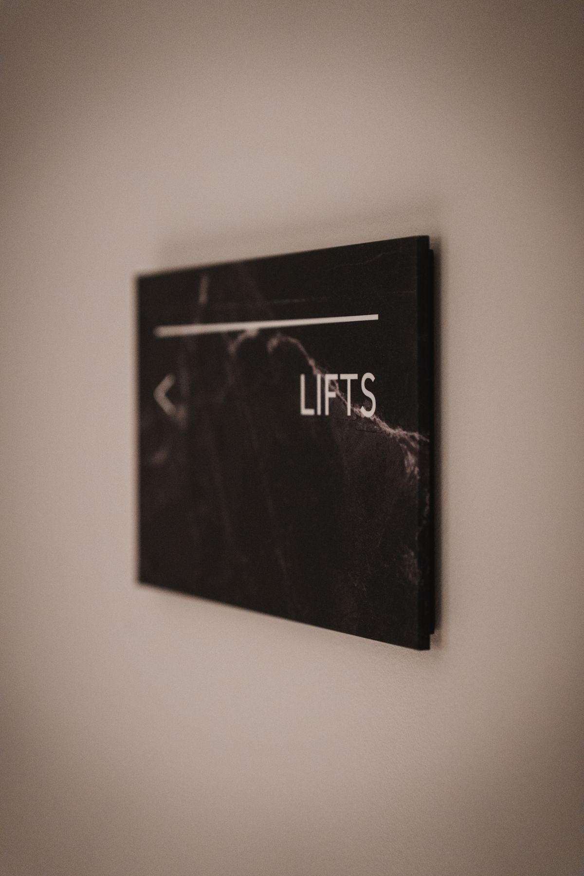 Wall-mounted directional acrylic plaque reading 'Lifts' with a marble-effect finish