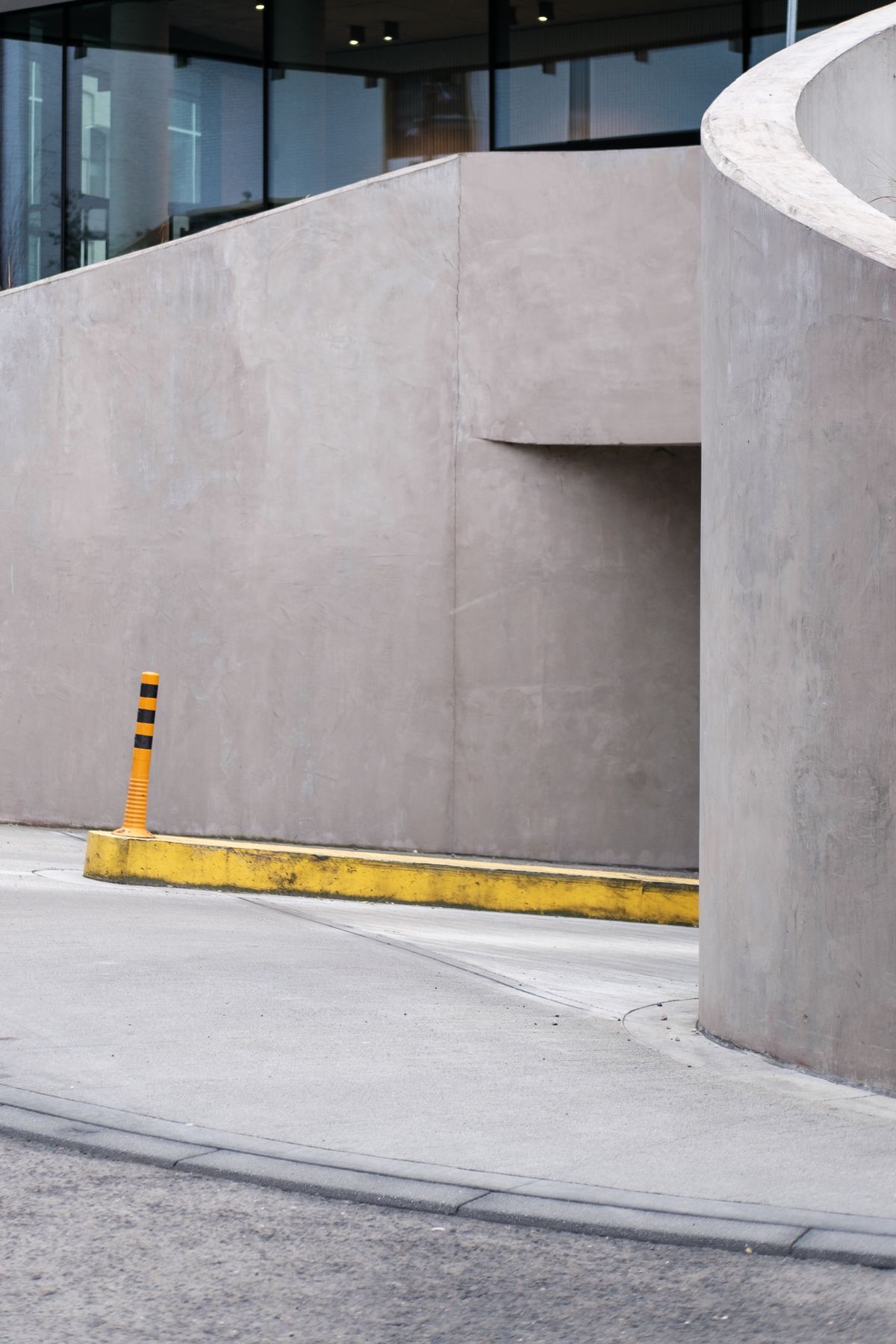 Single yellow and black bollard beside a modern concrete building entrance