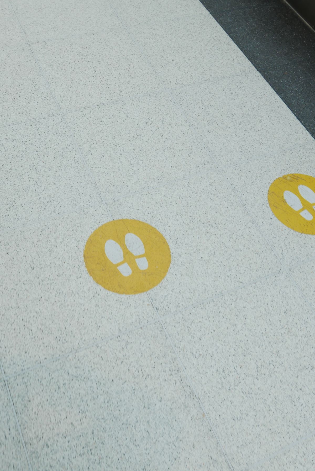 Yellow circular floor graphic decals with footprint icons on a tiled floor