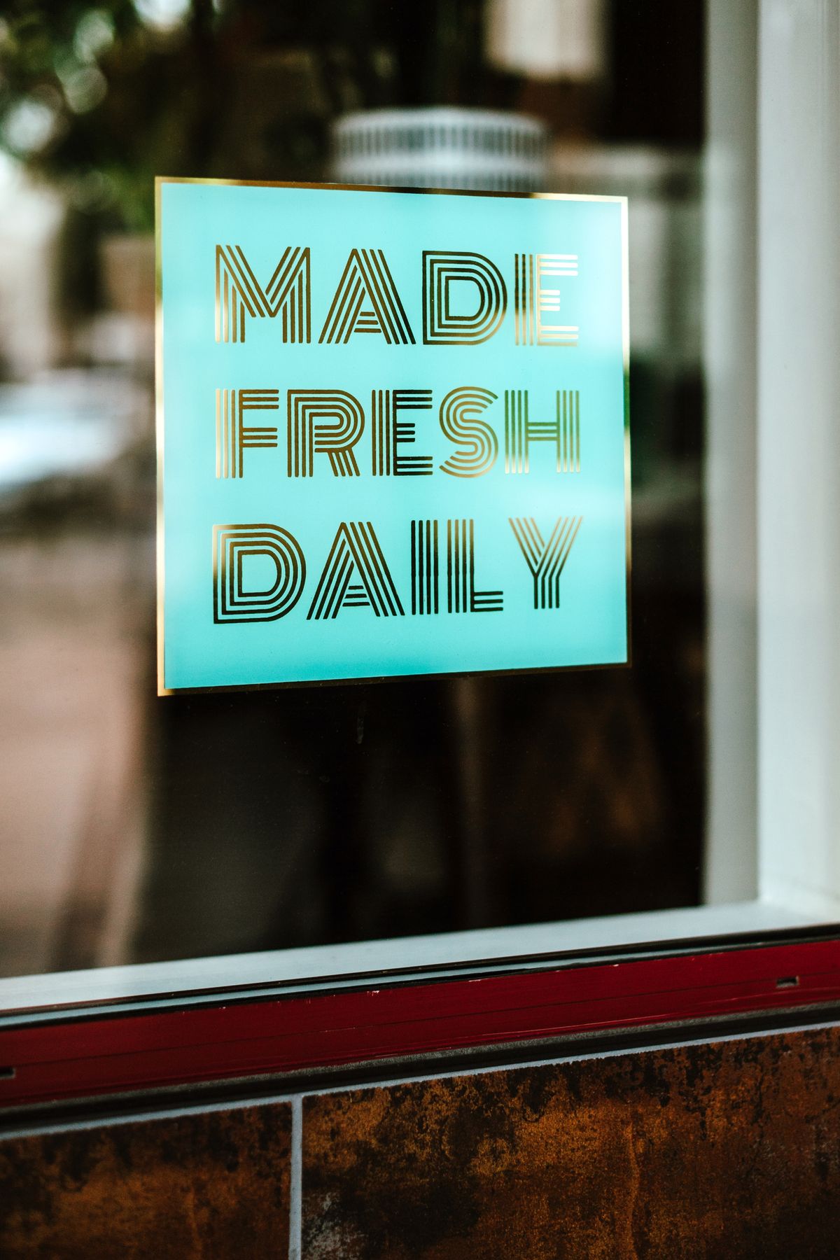 Turquoise and gold vinyl lettering reading 'Made Fresh Daily' on a shop window