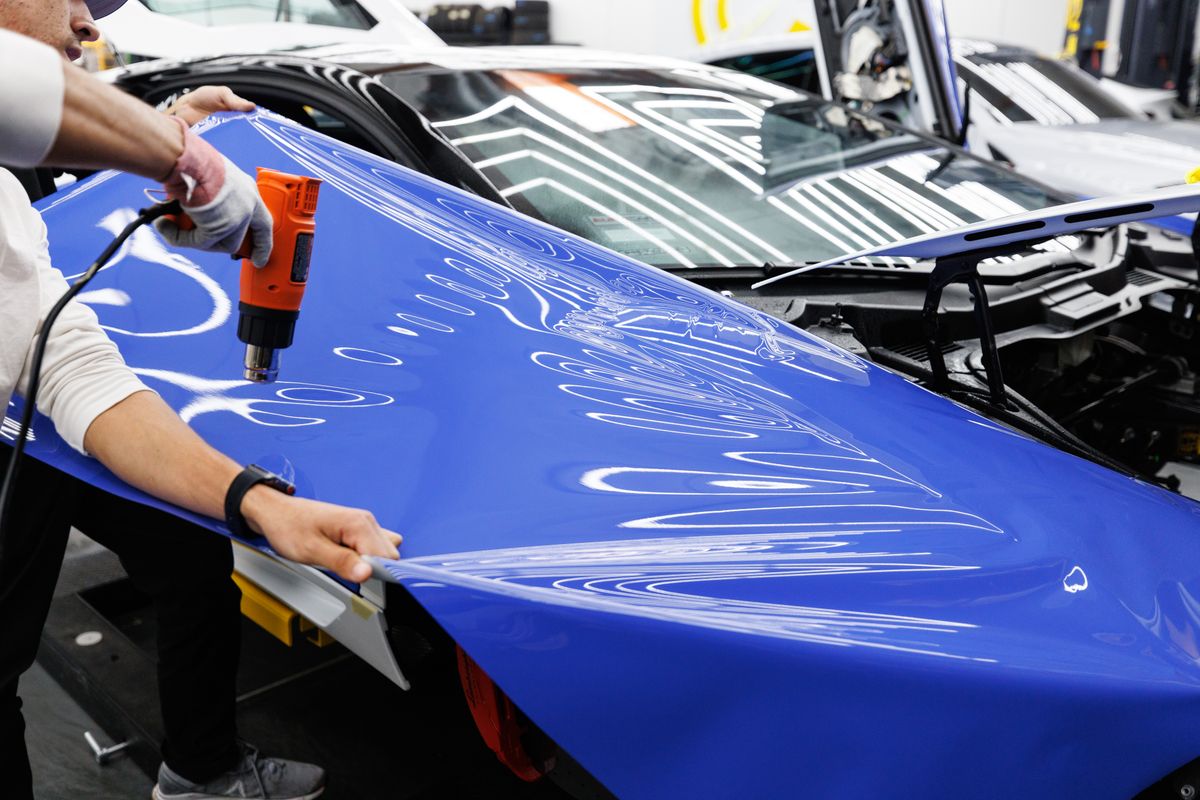 Installer applying a vivid blue vinyl wrap to a car bonnet with a heat gun