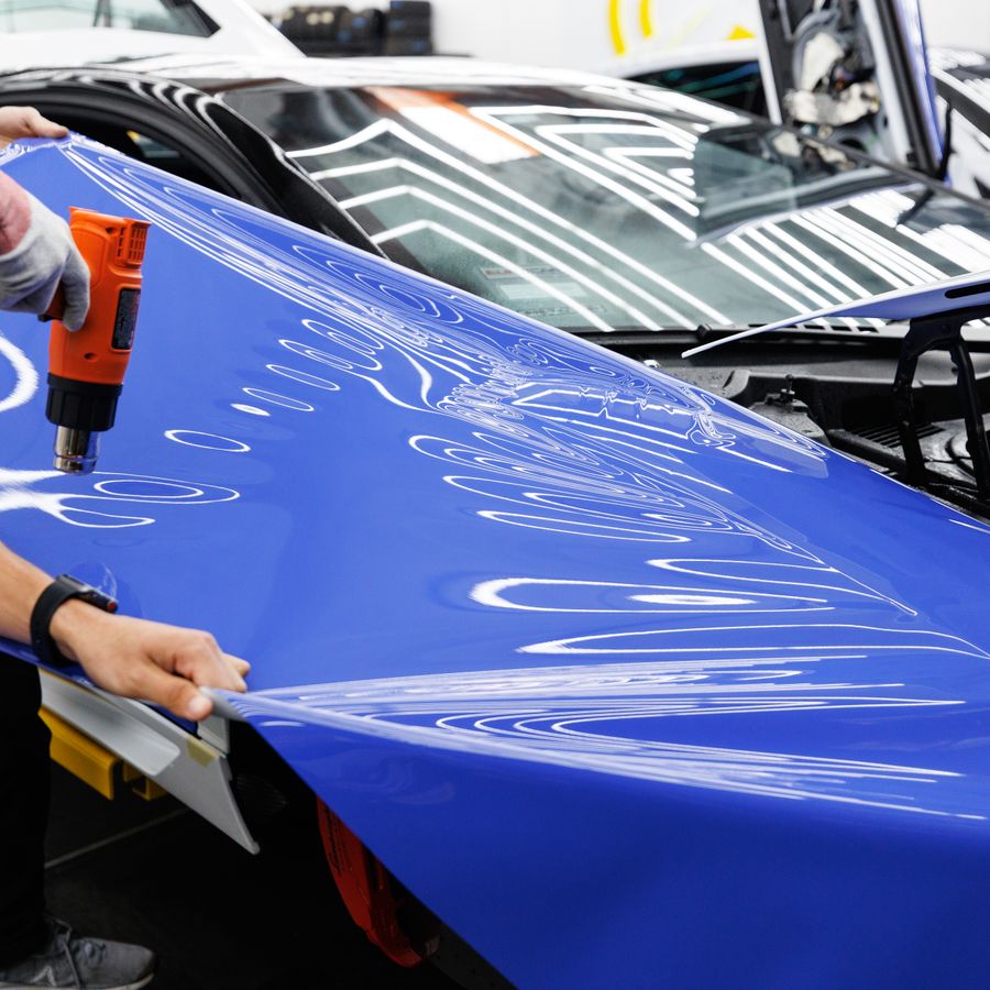 Installer applying a vivid blue vinyl wrap to a car bonnet with a heat gun