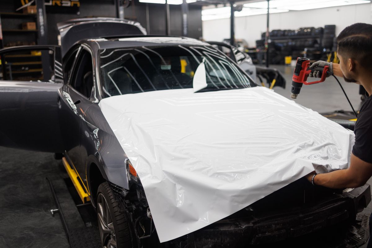 Technician using a heat gun to finish a full vehicle wrap on a white car in a workshop