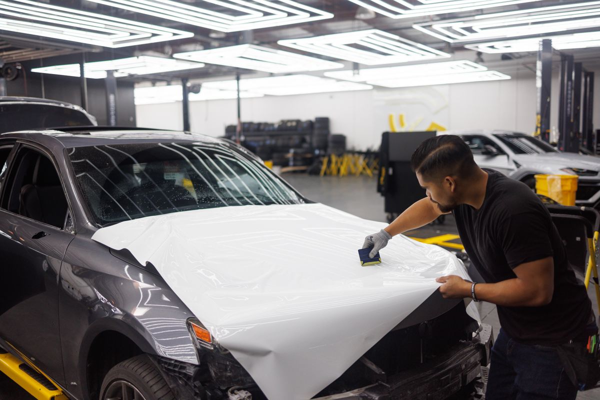 Installer wrapping a car bonnet with vinyl in an automotive workshop